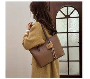Detail view of a large brown litchi pattern tote bag with a cute bear plush charm