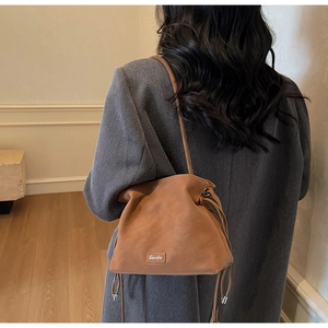 Rear view of a model wearing the brown drawstring bucket bag with a gray winter coat