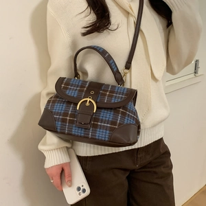 Detail of vintage blue plaid crossbody bag featuring leather trim and gold buckle on model
