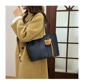 Detail of black pebbled leather tote bag featuring a cute brown plush bear charm and tassel