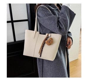 Detail of cream lychee leather tote bag with plush bear charm and woven tassel