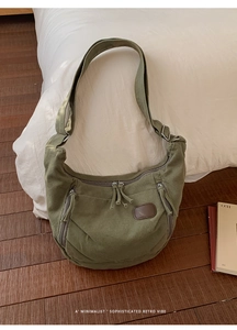 Macro view of dark green canvas hobo bag with multiple zipper pockets and brown leather patch