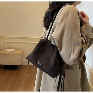 Detail of a dark brown suede bucket bag with drawstring closure and crossbody strap