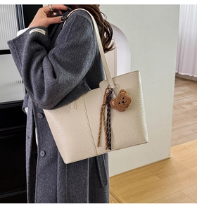 Detail of off-white tote bag with litchi texture and cute brown plush bear pendant