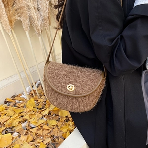 Borsa a sella marrone in peluche con chiusura dorata su sfondo di foglie autunnali