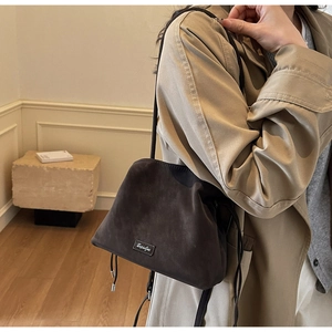 Detail showing the soft suede texture and silver logo plaque of the brown bucket bag