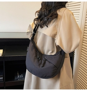 Detail of a black nylon crescent bag with adjustable strap and brand tag on a model