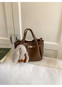 Detail of lychee pattern leather bucket bag with plush rabbit charm and metal twist lock