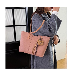 Detailed texture of pink pebbled leather tote bag with a plush bear charm on shoulder