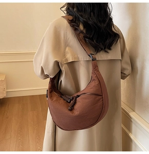 Close-up of brown crescent moon bag on shoulder with textured fabric and zipper detail