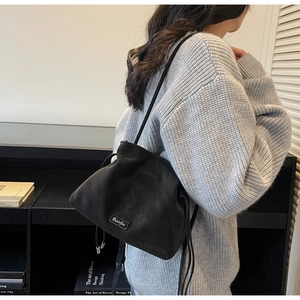 Matte black bucket bag with drawstring closure and slim shoulder strap on model