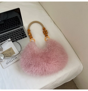 Détail du sac à main en peluche rose avec perles en bois et poignée en corde sur un lit blanc