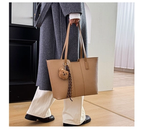 Detail of khaki tote bag with litchi texture featuring a plush bear charm and silk scarf
