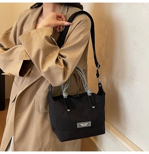 Détail du sac noir avec anse en corde tressée sur mannequin en trench-coat