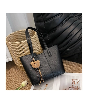 Close-up of black lychee grain leather tote bag with a brown bear plush pendant