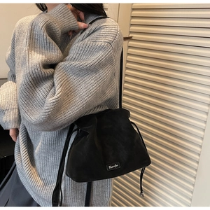 Detail of black suede bucket bag with drawstring closure and metallic logo plate