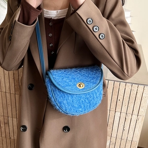 Dettaglio della borsa a sella in pelliccia blu con chiusura dorata su blazer marrone