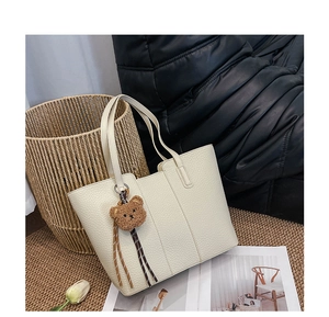 Detail of off-white lychee leather tote bag featuring a cute brown teddy bear charm