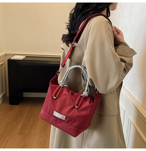 Détail d'un sac seau bordeaux avec poignées en corde tissée et large bandoulière en toile