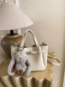 Chic beige lychee leather bucket bag with metal buckle and cute plush rabbit charm