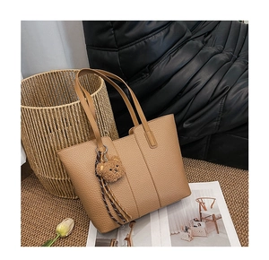 Detail of tan tote bag with lychee texture and cute bear charm in a cozy indoor setting