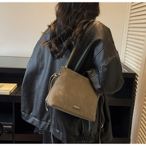 Close-up of khaki bucket bag with silver metal logo plaque and drawstring side detail