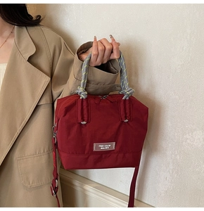 Détail du sac seau en nylon bordeaux avec poignée tressée bicolore et logo de marque