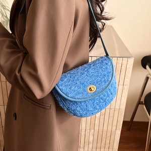 Borsa a sella in tweed blu con chiusura dorata indossata su un blazer marrone