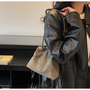 Detail of a brown matte suede bucket bag with drawstring and silver brand plaque