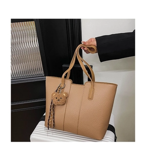 Macro view of textured camel leather tote bag with cute bear pendant on a white suitcase