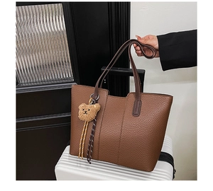 Close-up of brown litchi grain tote bag with bear charm on white striped suitcase
