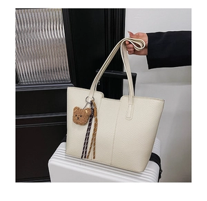 Detail of off-white lychee pattern tote bag with bear charm and woven tassel accent