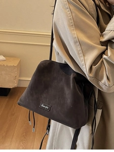 Minimalist matte suede drawstring bucket bag in dark coffee shown on a model's shoulder