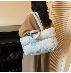 Detailed side view of large light blue quilted puffer tote bag worn by a model