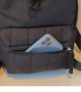Macro detail of quilted black nylon backpack featuring front zip pocket with smartphone