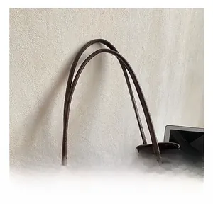 Detail of dark brown leather tote bag showing handle attachments and plush charm accessory