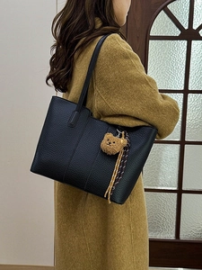Black pebbled leather tote bag with bear charm shown on model in yellow coat