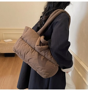 Detail of dark brown quilted puffer tote bag on shoulder showing large capacity and soft texture