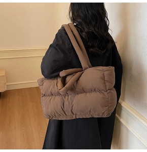 Quilted tote bag detail with thick padded handles shown worn over a black winter coat
