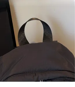 Close-up of the wide flat nylon carry handle and precise stitching on the black backpack