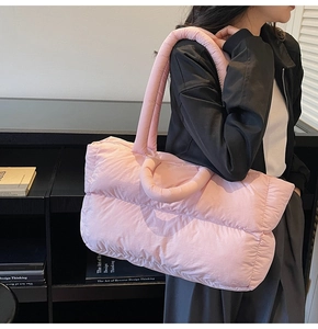 Close-up of light pink quilted puffer tote bag with dual straps worn by a model