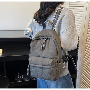Detail of dark gray quilted backpack with 'Have A Nice Day' woven strap and dual zippers