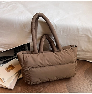 Close-up of a large quilted down tote bag in dark brown on a wooden floor
