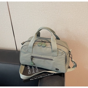 Detail view of olive green waterproof nylon crossbody bag on a black leather bench