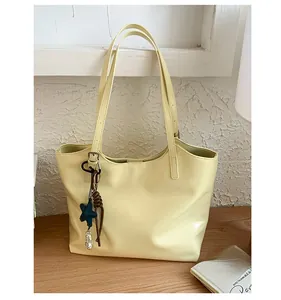 Détail d'un sac cabas en cuir jaune crème avec un charme étoile sur une table en bois