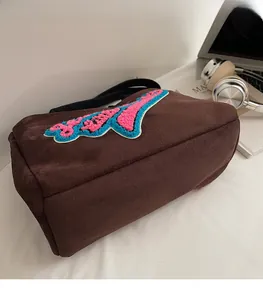 Détail du sac à bandoulière en peluche marron avec broderie sur un décor de bureau