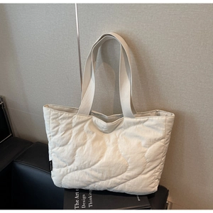 Detail of cream quilted tote bag showing wave stitching and brand label on nylon surface