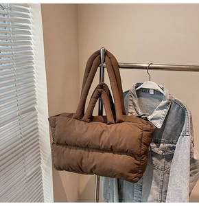 Detail of dark brown quilted tote bag showing padded handles on metal display