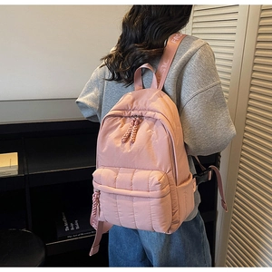 Detail of pink quilted backpack showing puff fabric texture and woven rope zippers