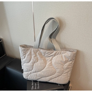 Detail of light grey quilted tote bag with wavy stitching on a black leather bench